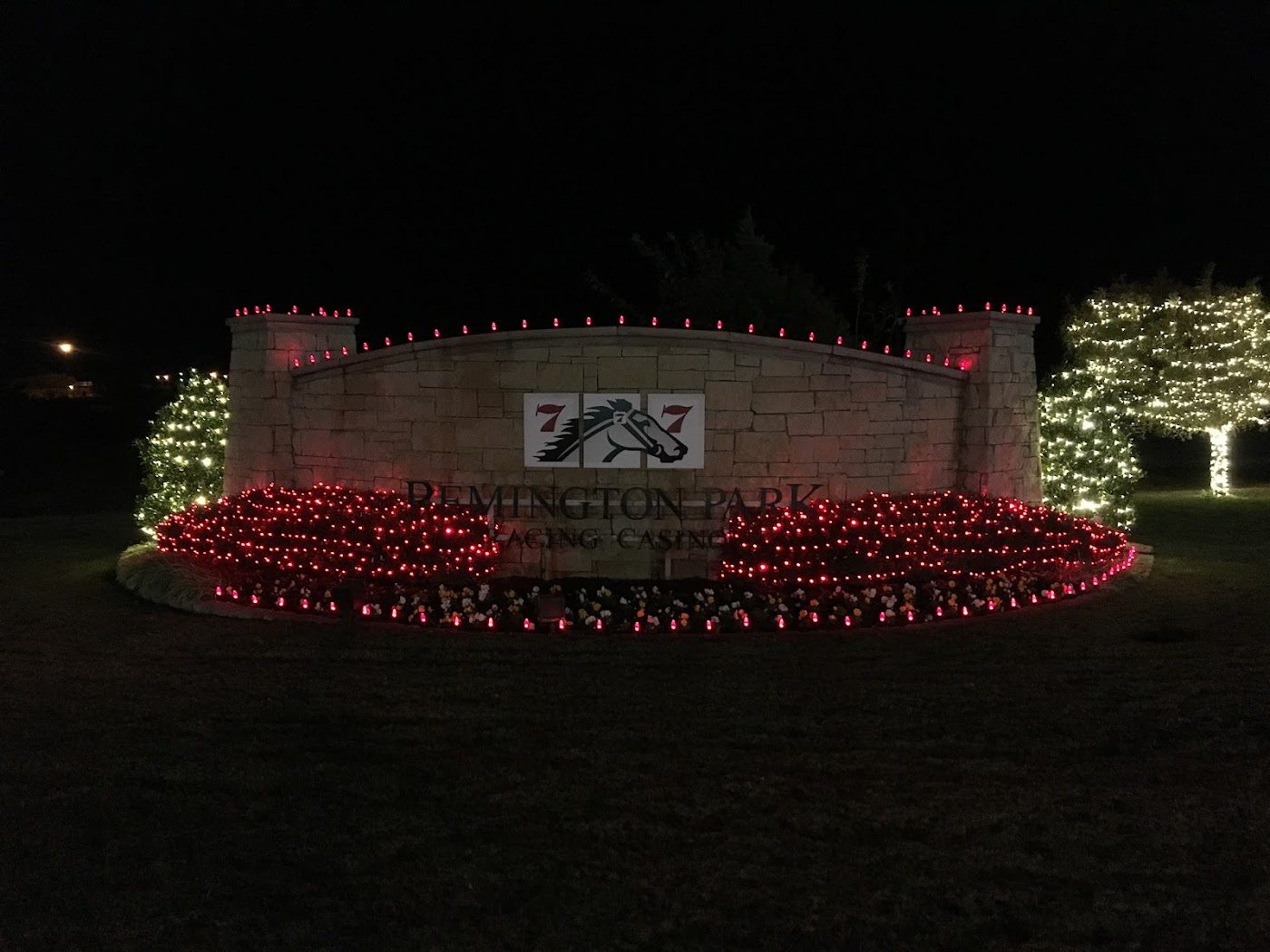 A large stone entrance sign at Remington Park lit with red and white holiday lighting