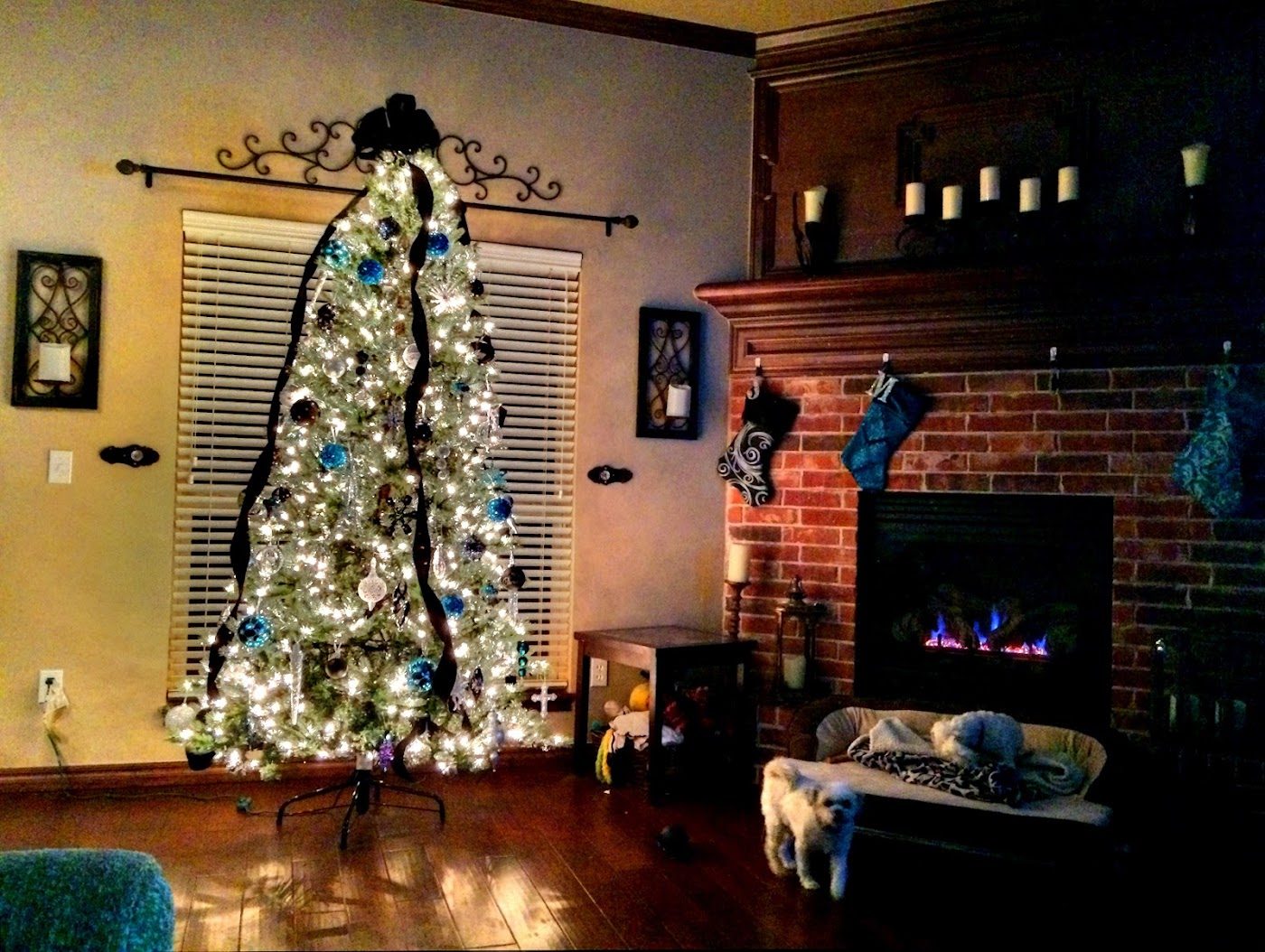 A decorated and lit Christmas tree beside a brick fireplace