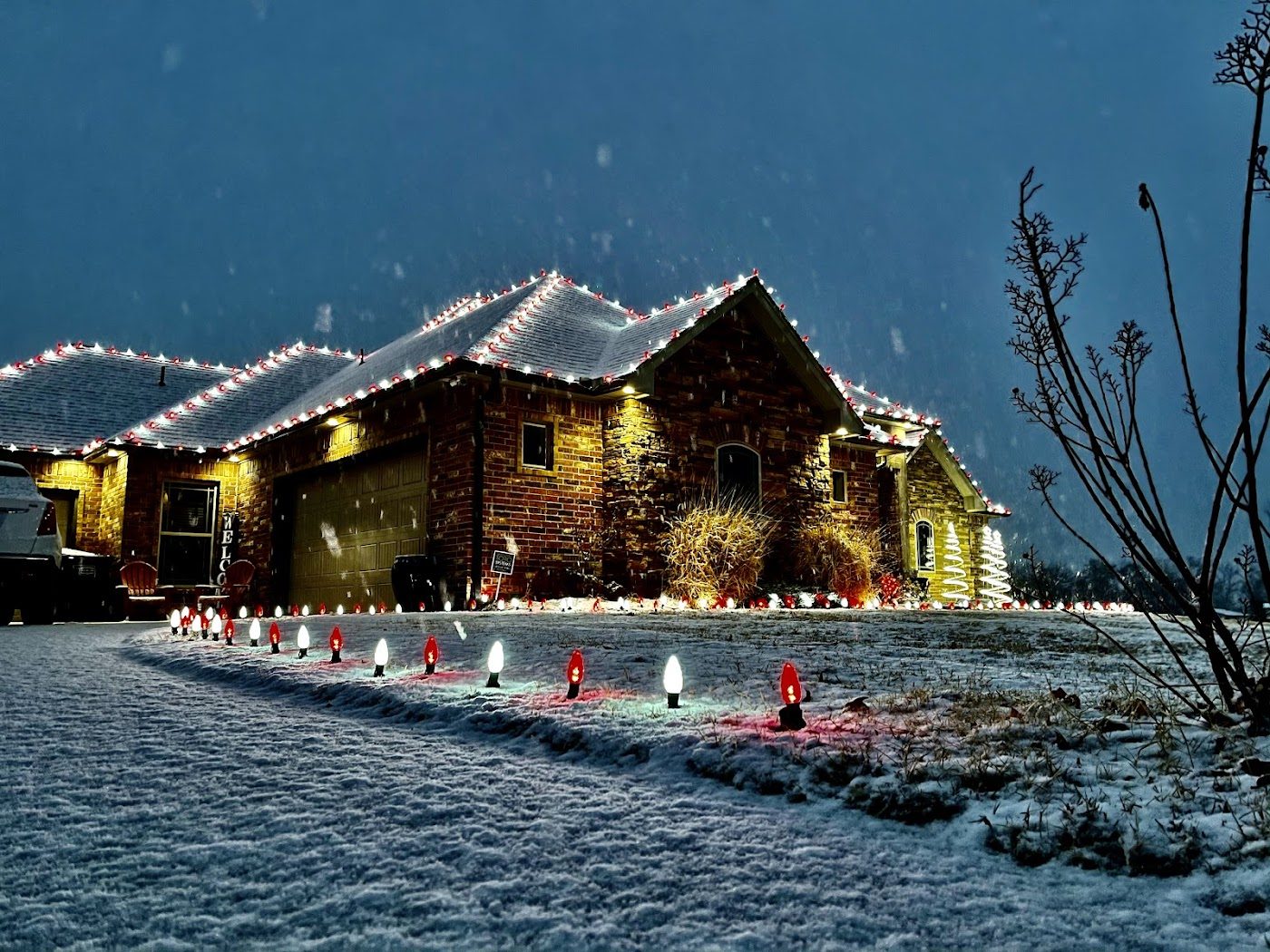 A home outlined in red and white roofline lights with a lit pathway in light snow